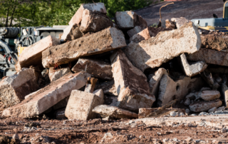 Excavating & Grading Waukesha WI - Pile of concrete rubble at a demolition site with heavy machinery in the background.