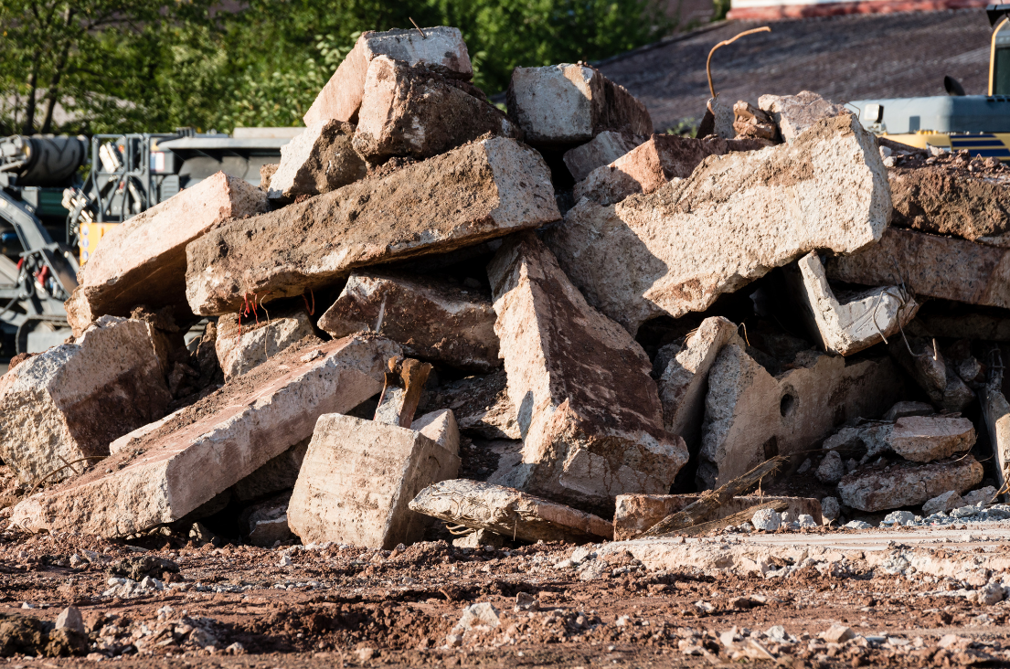 Excavating & Grading Waukesha WI - Pile of concrete rubble at a demolition site with heavy machinery in the background.